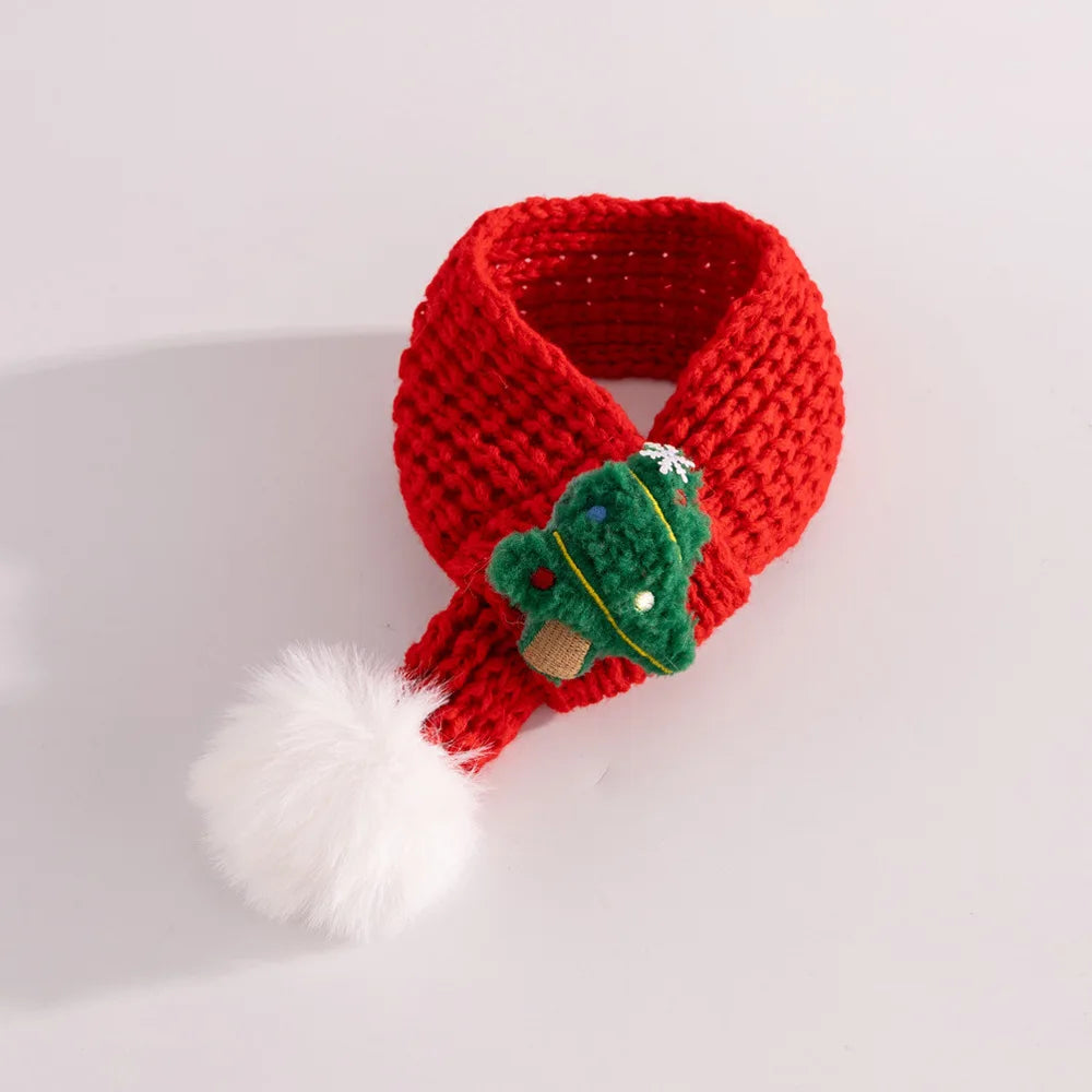 Red knitted scarf with a green leaf and white pom-pom on a light gray background