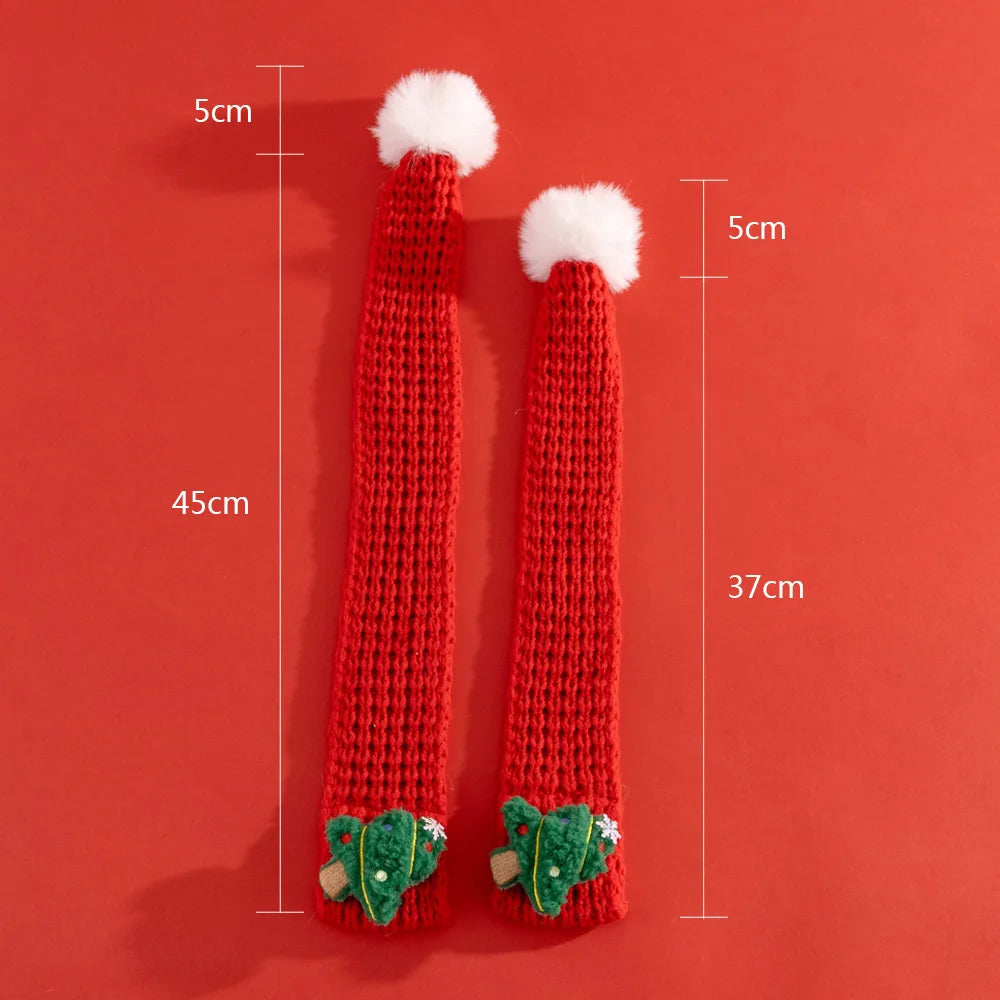 Red knitted leg warmers with white pom-poms and green leaf details on a red background, showing measurements.