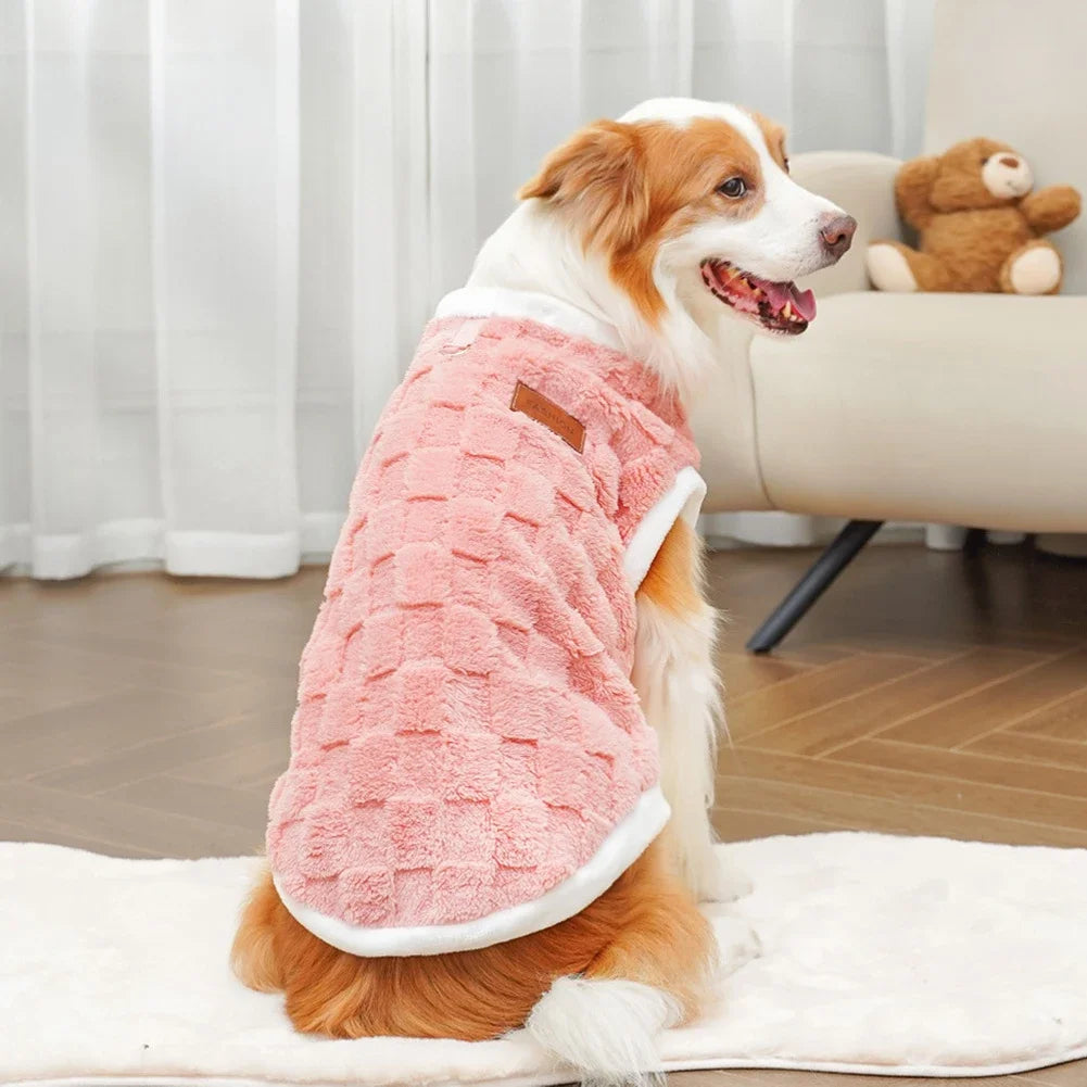 Dog wearing a pink robe sitting on a white blanket in a living room.