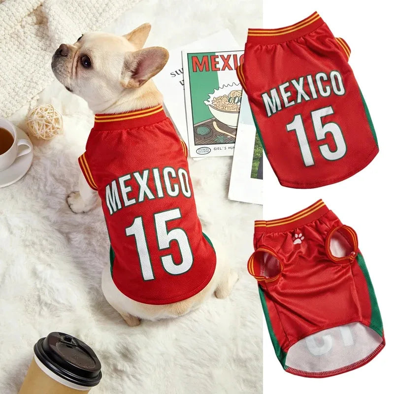Dog wearing a red 'Mexico 15' jersey on a white surface with a magazine and coffee cup in the background.