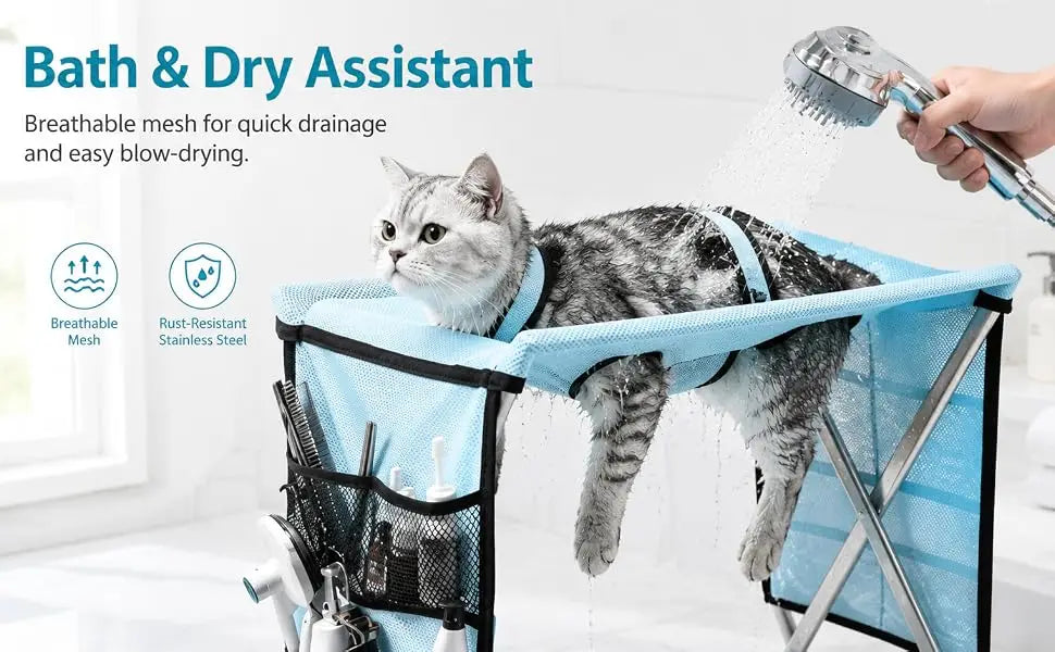 A gray tabby cat sits in a blue mesh bath and dry assistant chair while a hand holds a shower head spraying water. The chair has black trim, a side storage pocket with grooming tools, and text on the left describing breathable mesh and rust-resistant stainless steel.