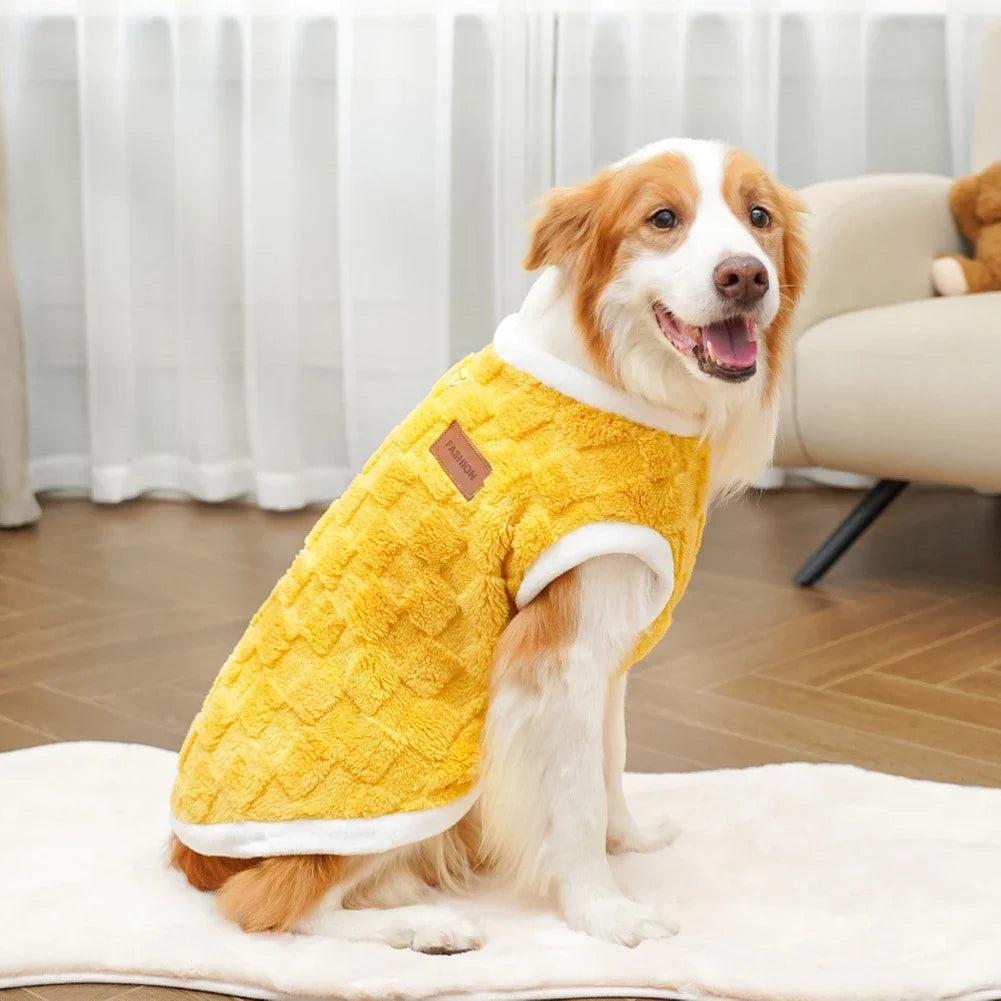 Dog wearing a yellow quilted coat sitting on a white blanket in a living room.