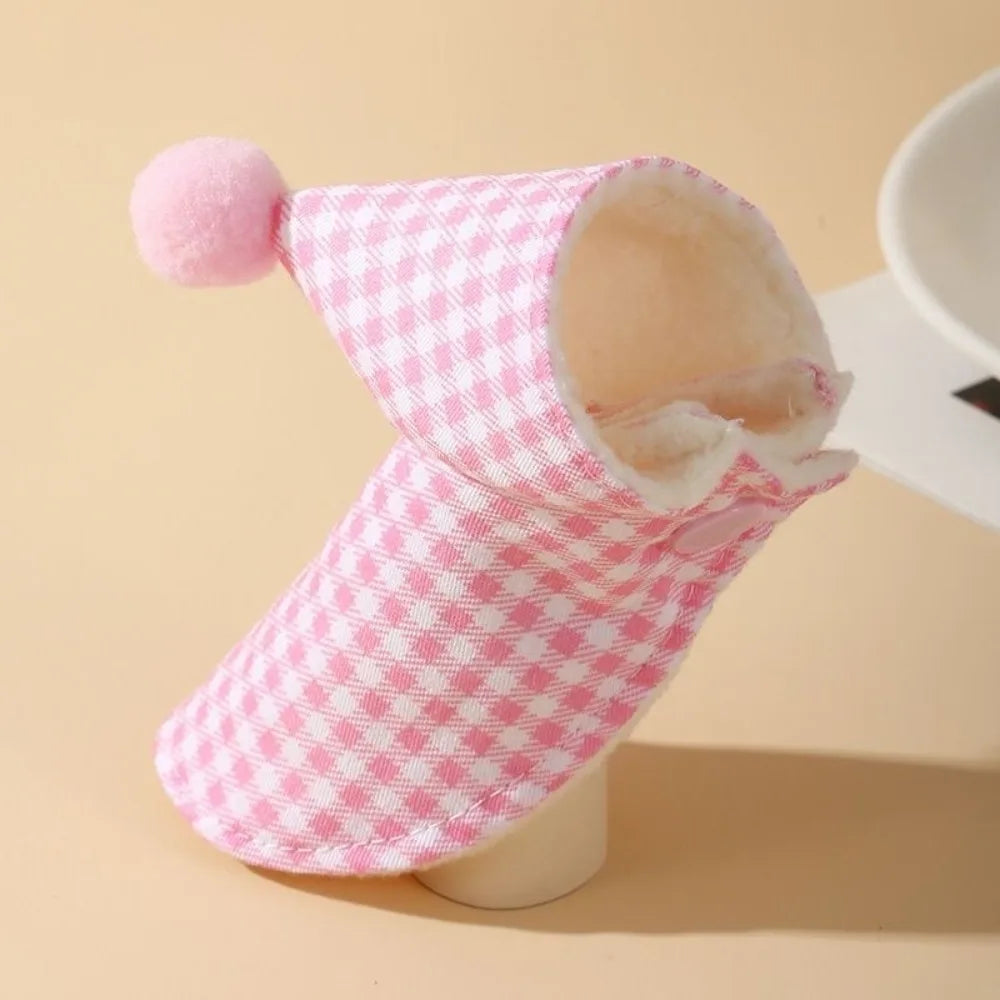 A pink and white gingham baby bootie with a soft cream-colored fleece lining and a matching pink pom-pom on the cuff, displayed on a beige mannequin stand.
