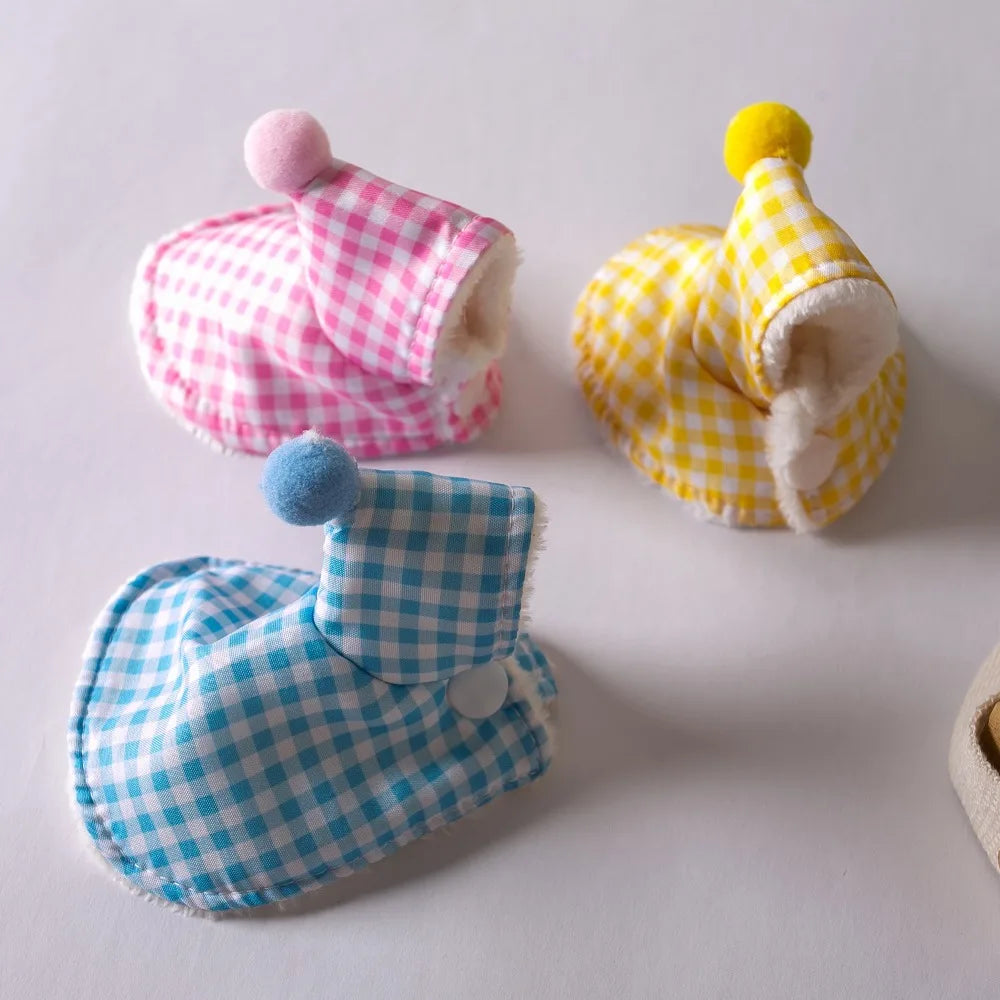 Three small checkered fabric booties or bootie covers arranged on a light gray background, each with a pom-pom on top: one pink and white, one yellow and white, and one light blue and white.