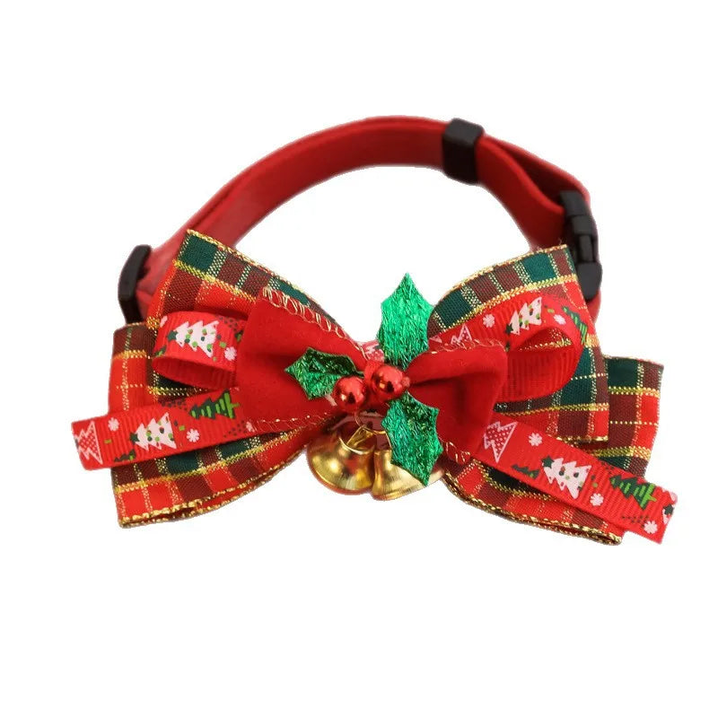 A red pet collar with a large Christmas-themed fabric bow featuring red, green, and gold plaid patterns, a green glittery holly leaf, small red berries, and a gold bell in the center.