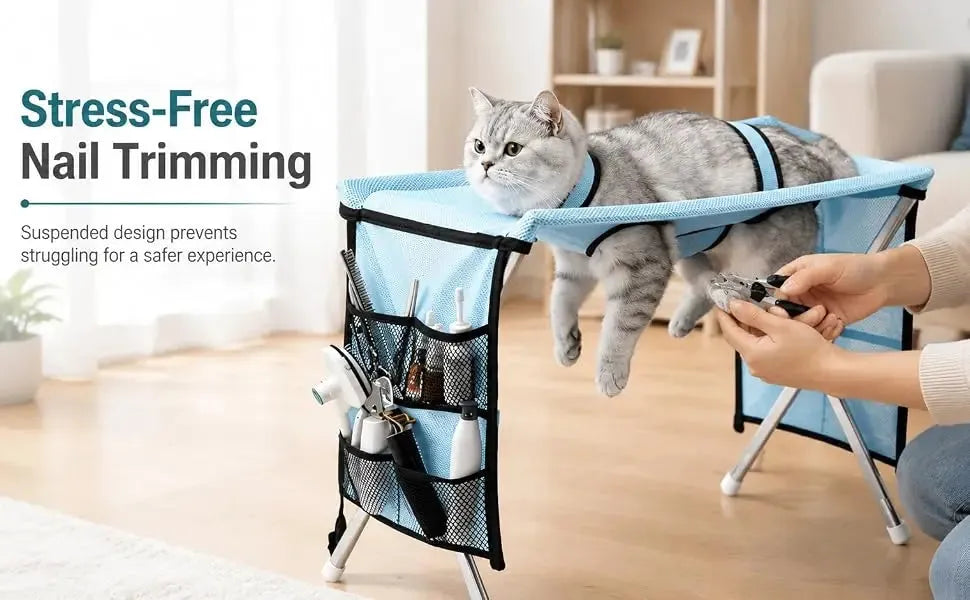 A gray cat lies on a blue and black pet nail trimmer stand while a person holds nail clippers. The stand has mesh side pockets holding grooming tools.