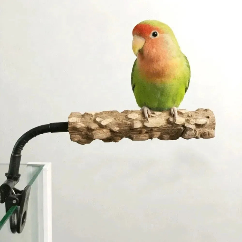 A small green lovebird with a peachy face perched on a textured wooden branch attached to a black clip, shown against a plain light background.