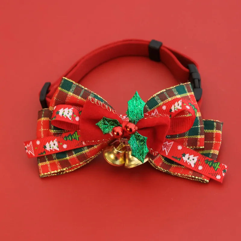 A red pet collar with a large decorative holiday bow made of red, green, and gold plaid ribbons, a red bow, green glitter holly leaves, and two small gold bells, shown on a solid red background.