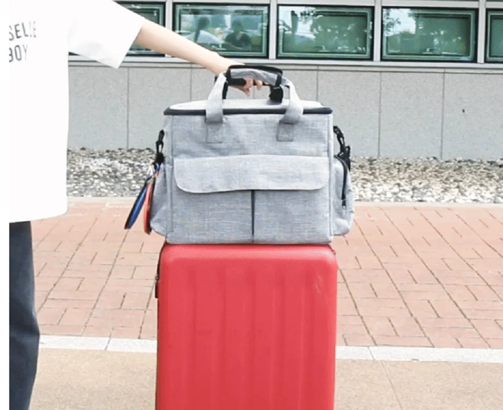Person holding a gray backpack over a red suitcase on a sidewalk.