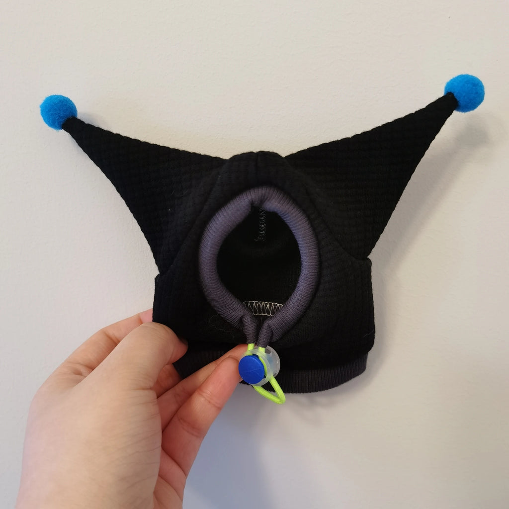 Black dog muzzle with blue pom-poms held by a hand on a light gray background