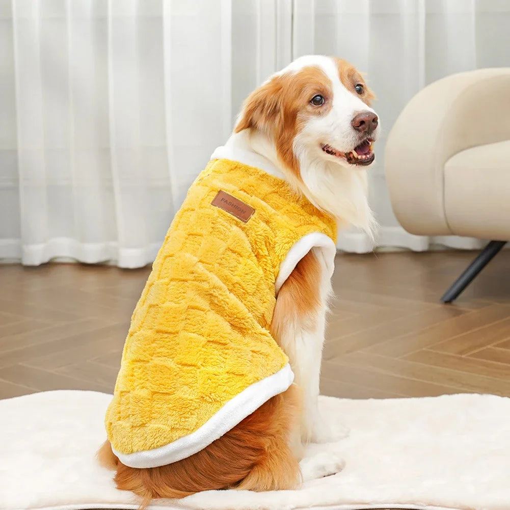 Dog wearing a yellow fleece coat indoors on a wooden floor.