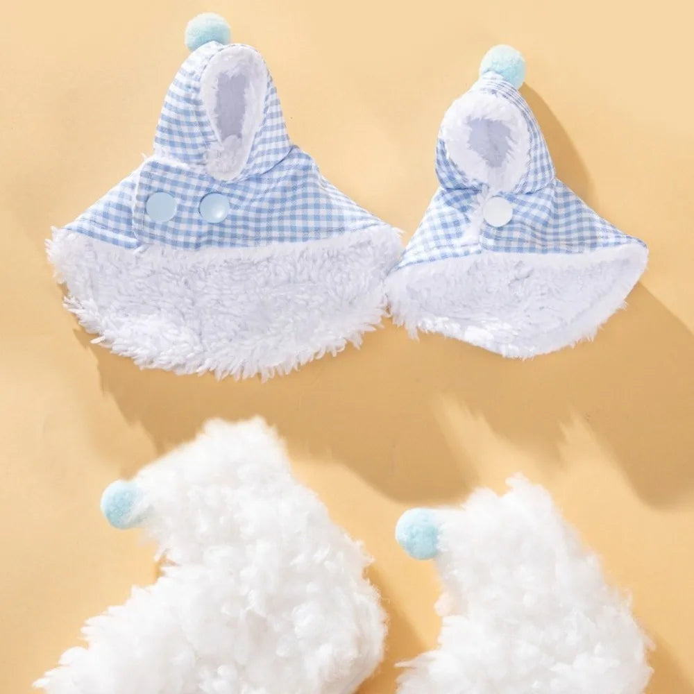 A set of baby accessories including two blue and white gingham bonnet hats with white faux fur trim and pom-poms, and two fluffy white booties with light blue pom-poms, arranged on a warm beige background.