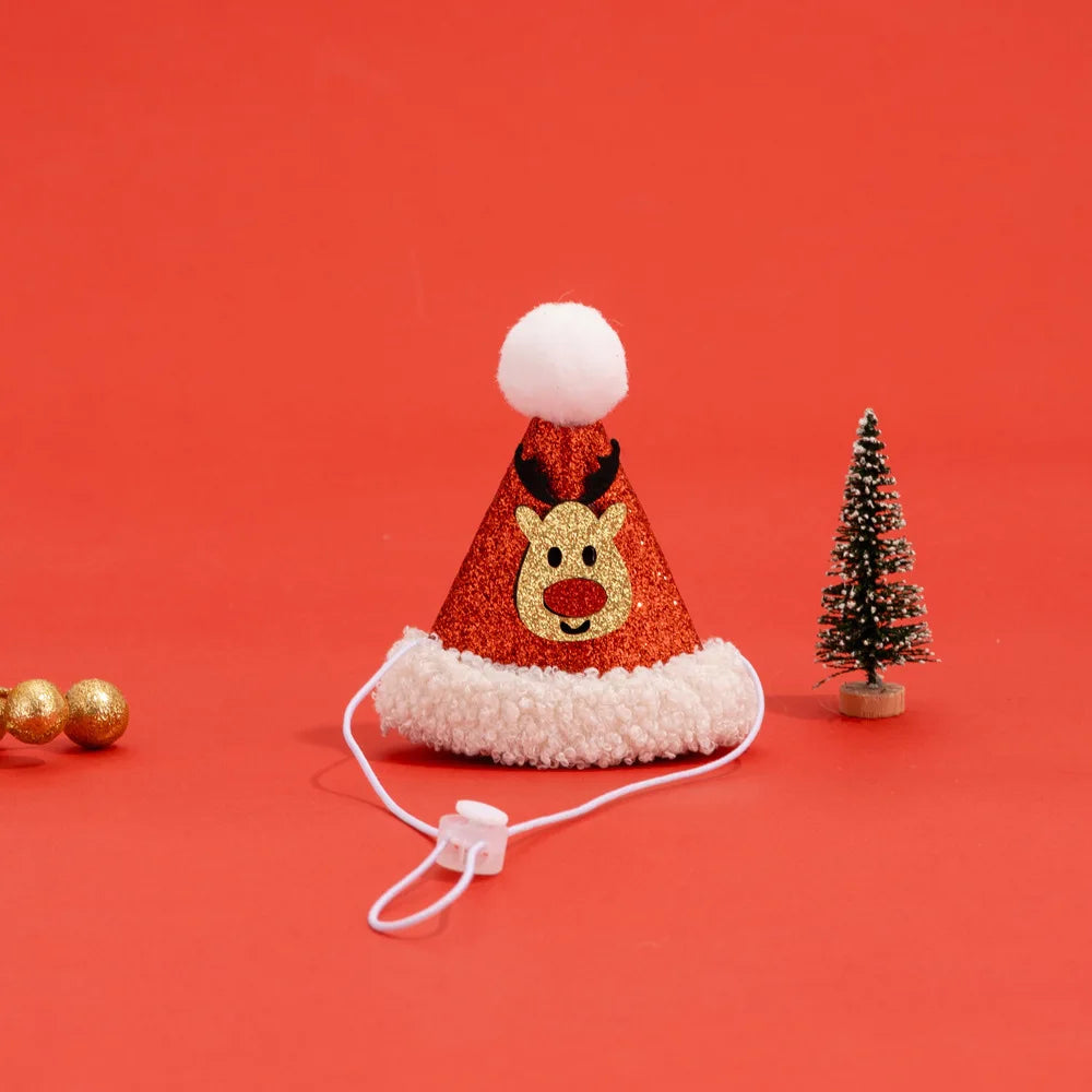 A festive Christmas party hat with a red glitter cone, white faux fur trim, a white pom-pom, and a glittery gold reindeer face. It features a white elastic chin strap with a plastic toggle, set against a solid red background with miniature holiday props.
