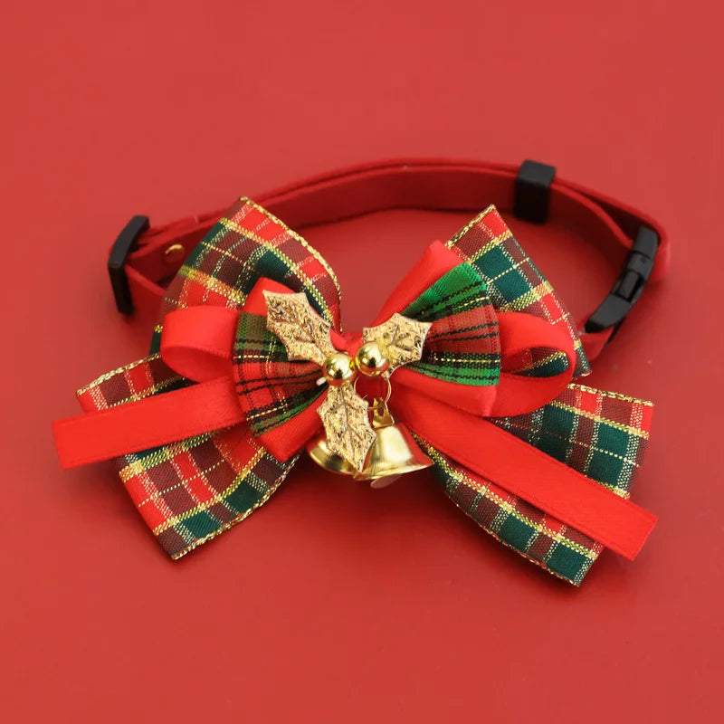 A red pet collar with a large Christmas-themed bow featuring red and green plaid fabric, red satin ribbons, a gold holly ornament, and a small gold bell, set against a solid red background.
