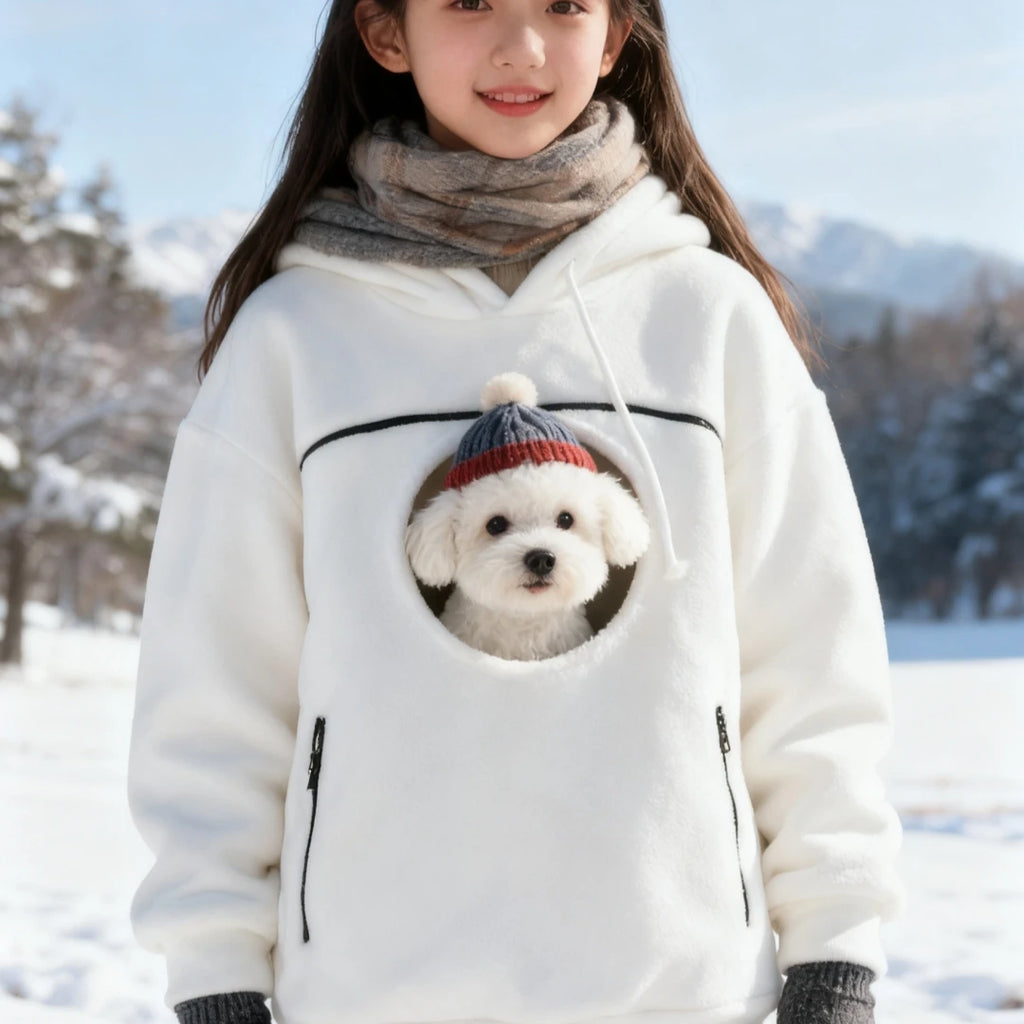 Person wearing a white hoodie with a dog inside a pocket, standing in a snowy landscape.
