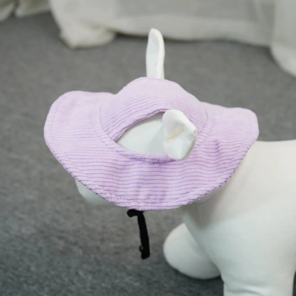 A light purple ribbed fabric pet hat with white faux fur ears and a black chin strap, shown on a white dog mannequin against a gray carpet background.