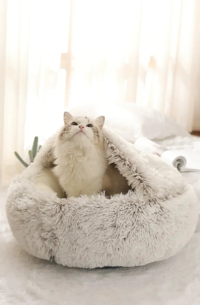 Cat sitting inside a fluffy beige pet bed with a soft white background