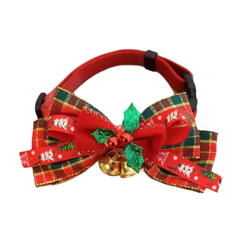 A red pet collar with a large Christmas-themed bow made of red, green, and gold plaid ribbons, decorated with a small green holly leaf, red berry ornament, and two gold bells, shown on a plain white background.