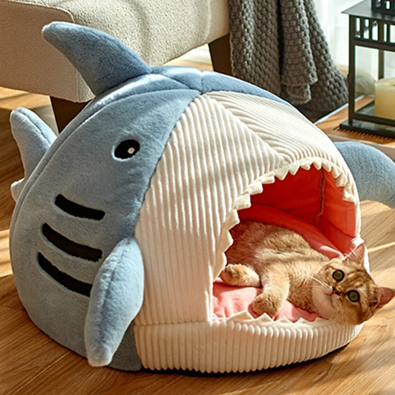 Cat lying inside a shark-shaped pet bed on a wooden floor.