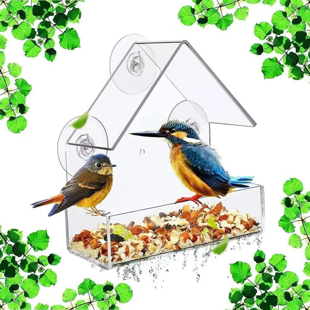 Clear bird feeder with birds perched on it, surrounded by green leaves.