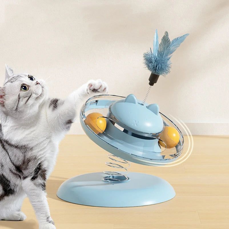 Cat playing with a spinning toy featuring feathers and balls on a beige background