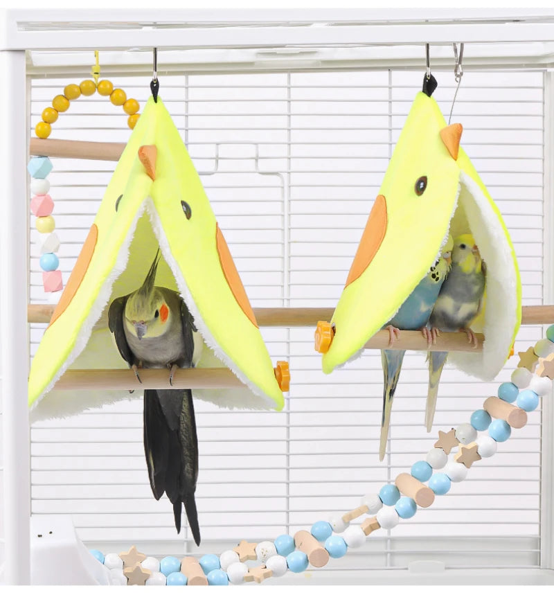 Two parakeets on yellow bird perches with a colorful beaded chain in front of white blinds.