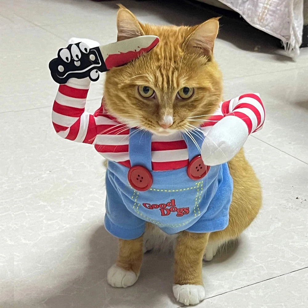 Cat wearing a costume with red and white striped shirt, blue overalls, and white gloves on a light-colored floor.