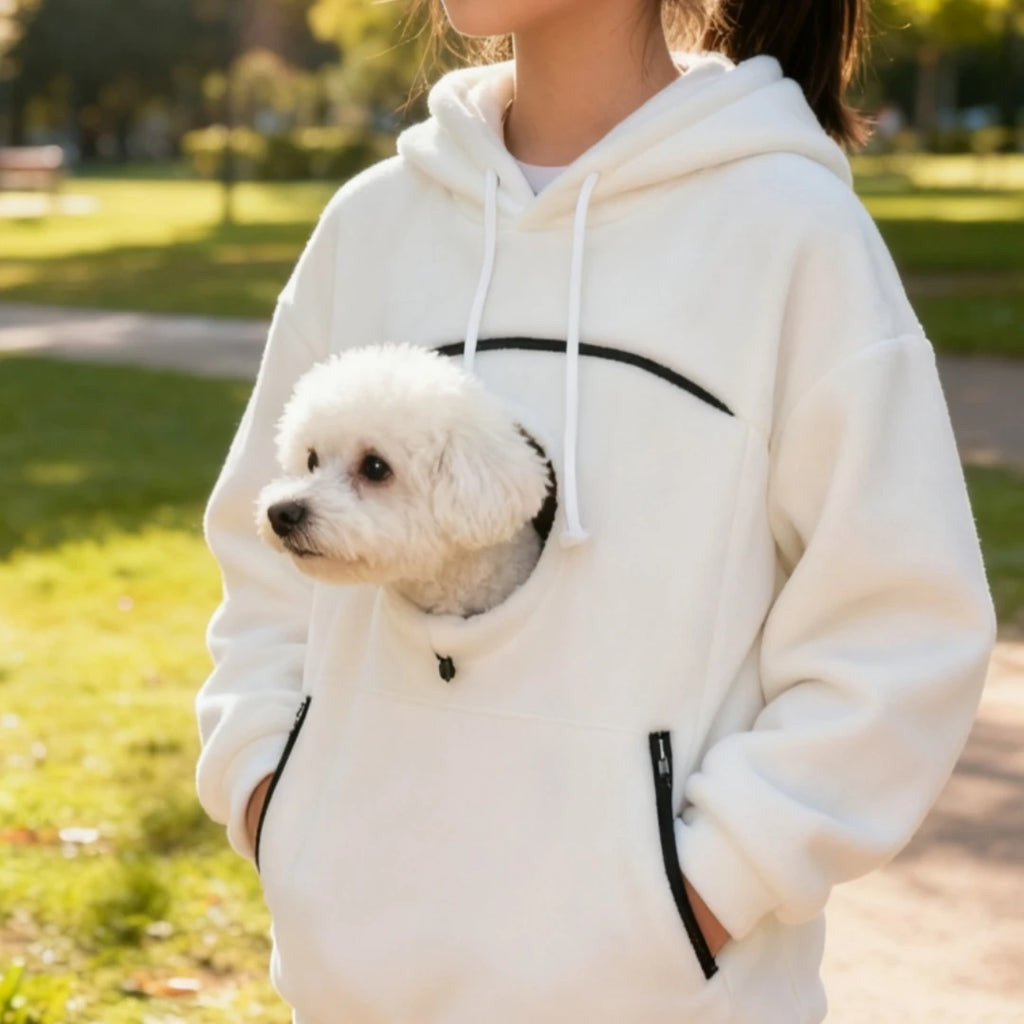 Person wearing a white hoodie with a small dog peeking out in a park setting