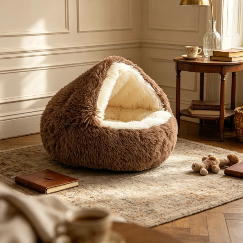 A plush, dome-shaped pet bed in a warm brown faux fur material with a cream-colored fleece interior, styled in a cozy, sunlit room on a patterned rug next to a wooden side table.